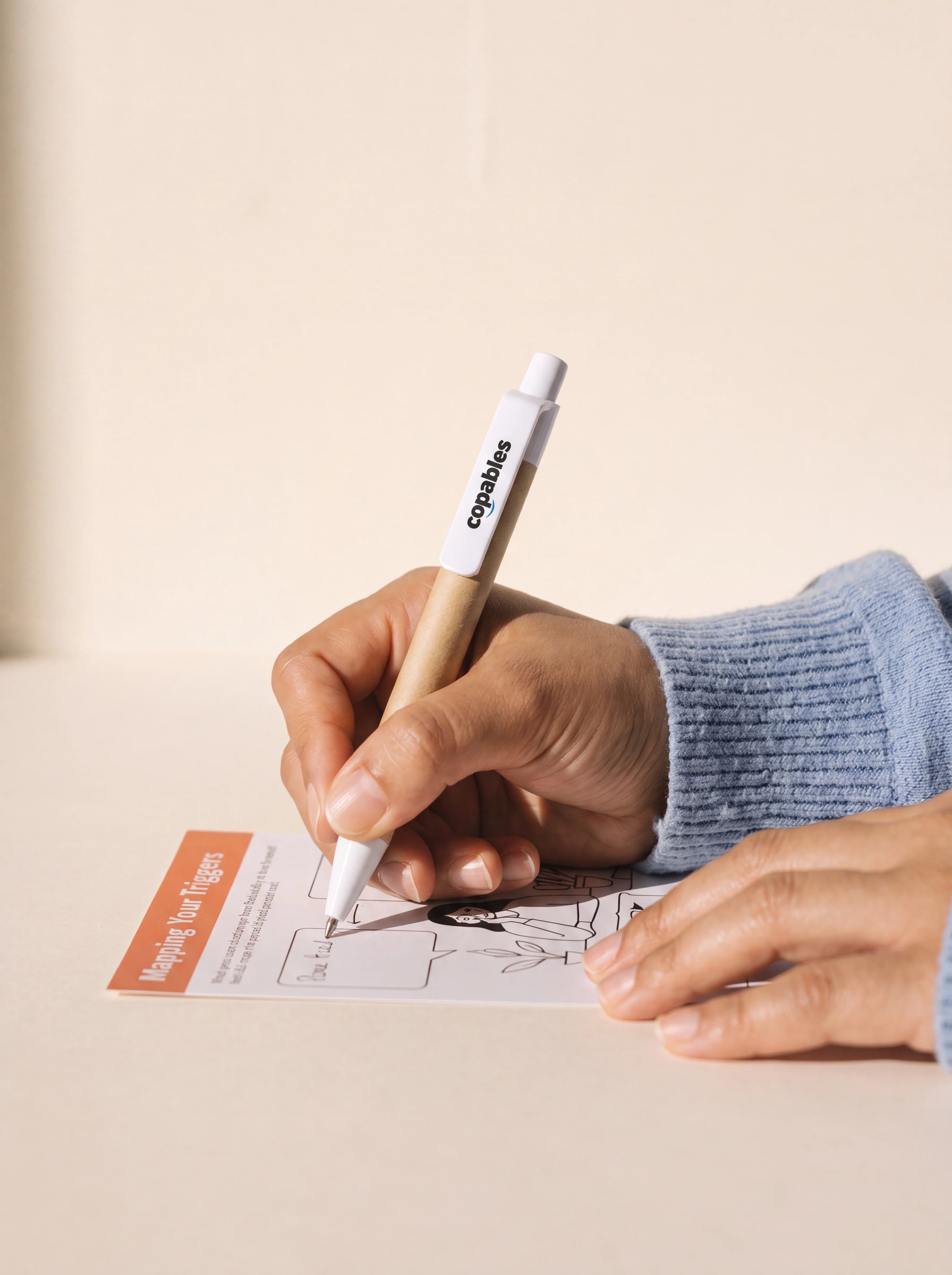 A hand writing on a Copables 'Mapping Your Triggers' protocol card with a copables-branded pen.