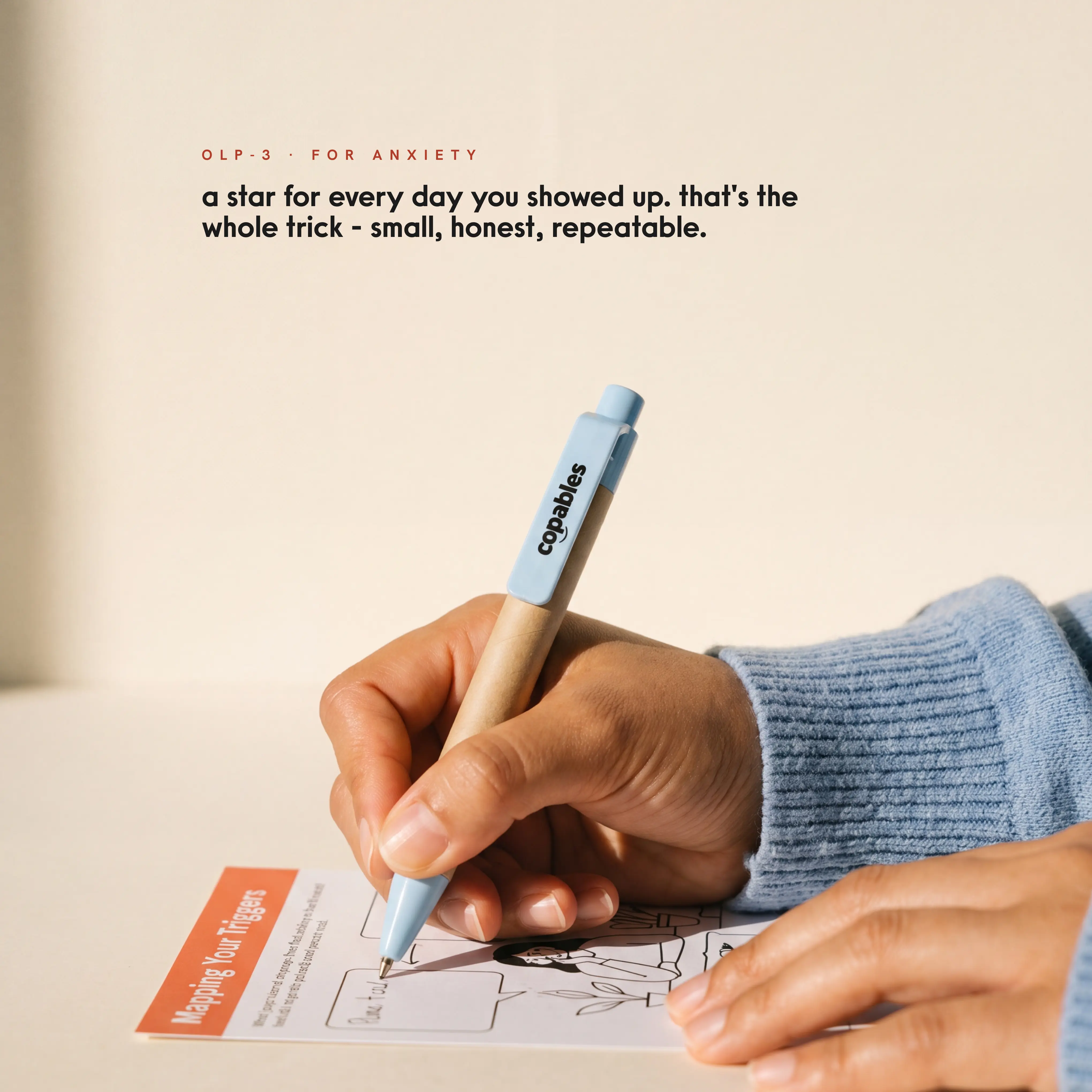 A hand writing on a Copables 'Mapping Your Triggers' protocol card with a copables-branded pen.